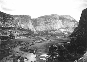 This photograph, taken in the early 1900s before the O'Shaughnessy Dam was constructed, shows the Hetch Hetchy Valley and the Tuolumne River, looking east.